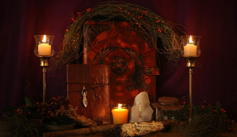 An altar with a large book, two candles, stones, and a bough.