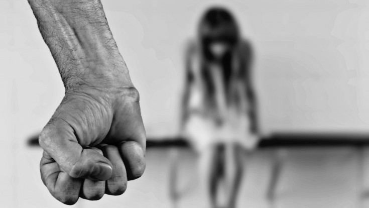 In the foreground, a clear fist. In the background, a person looking down, afraid.