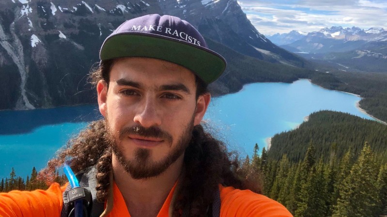 A picture of our instructor Adam in front of a lake in the Rockies. Adam's hat reads: "Make racists afraid again."