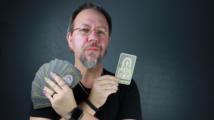 Instructor Lee Harrington holding up a spread out tarot deck with one card in the other hand.
