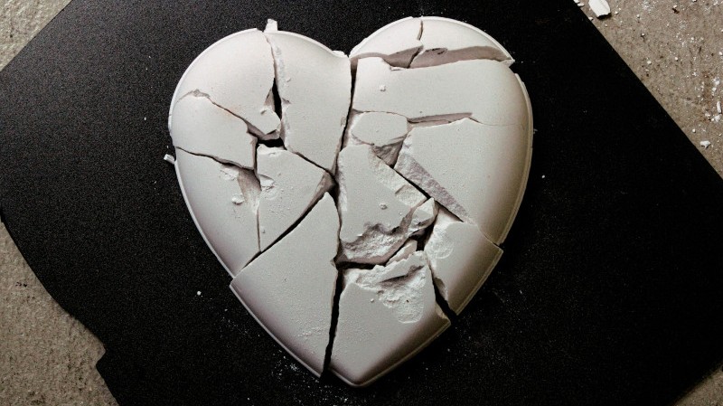 An image of a broken white ceramic sculpture of a heart, against a black background.
