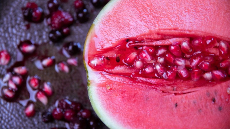 Image of a split watermelon with pomegranate seeds spilling out from inside.