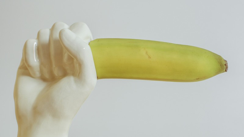 A white ceramic hand holding a banana horizontally toward its right side.