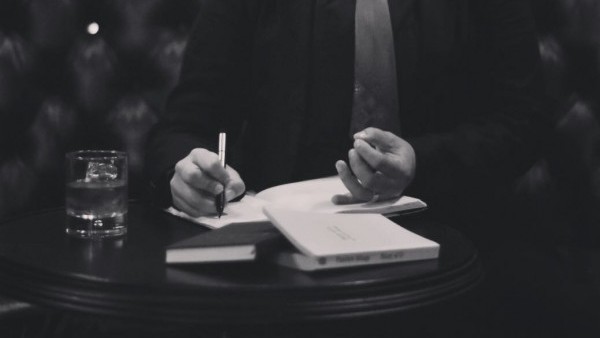 An image of Sinclair Sexsmith writing in a notebook wearing a tie.